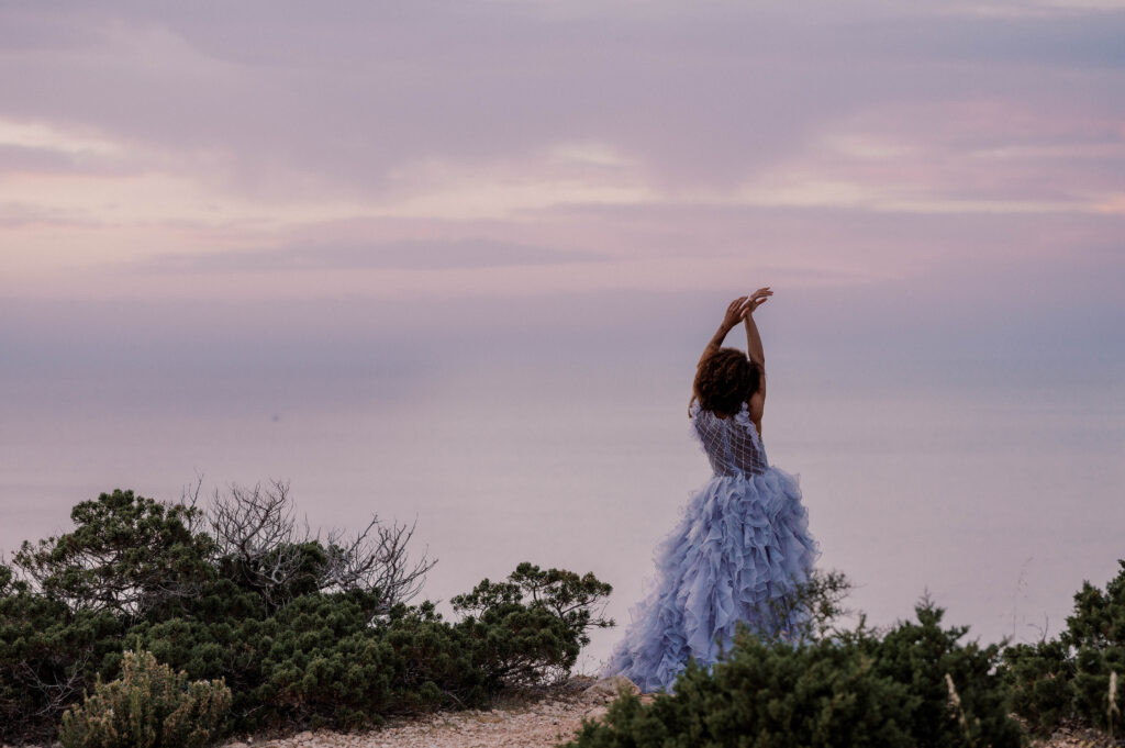 Bride looking out across the sea from atop a cliff, against a backdrop of purple and violet skies