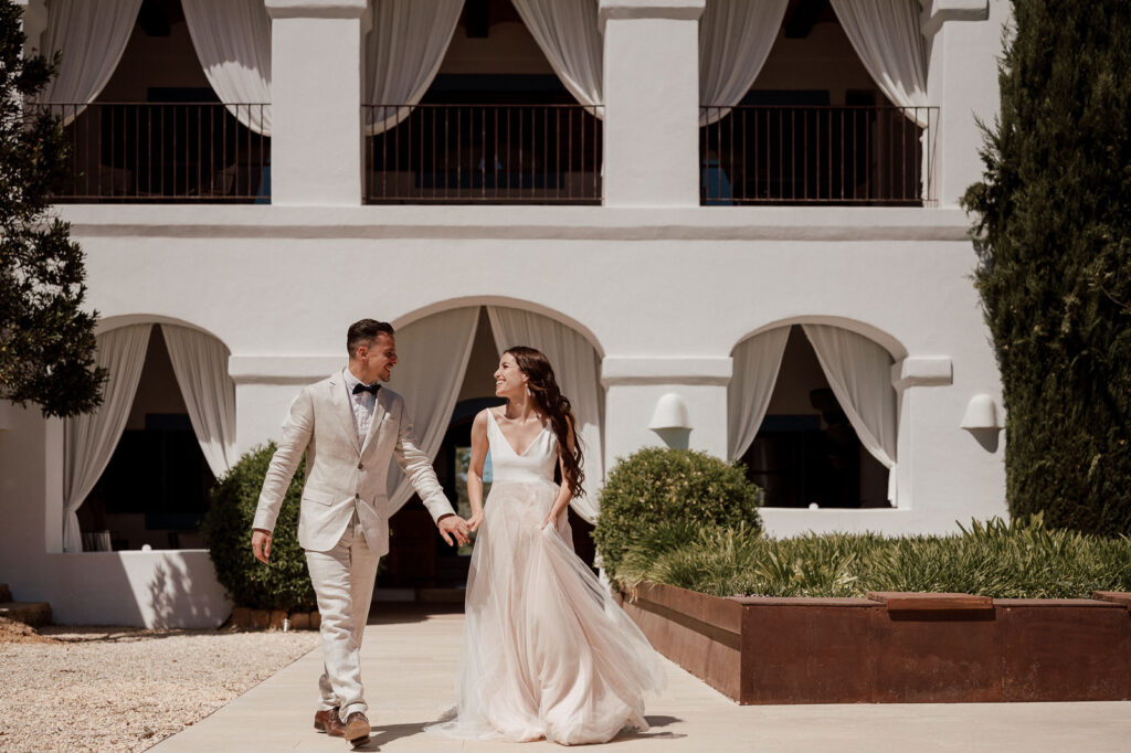 Couple strolling through the garden of a beautiful Ibiza wedding venue, holding hands and smiling at each other