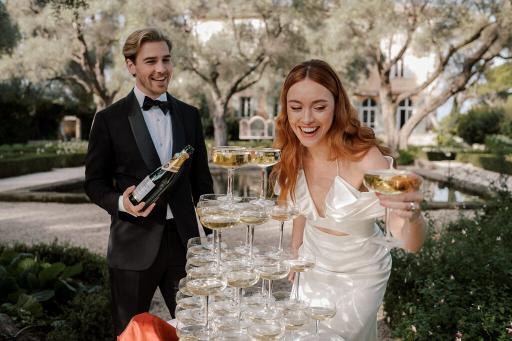 couple drinking champagne from tower in front of luxury venue in france